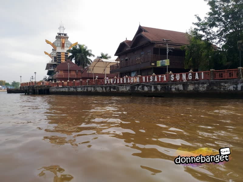 Rumah panggung kayu di tepi sungai di Banjarmasin, dilihat dari atas perahu.